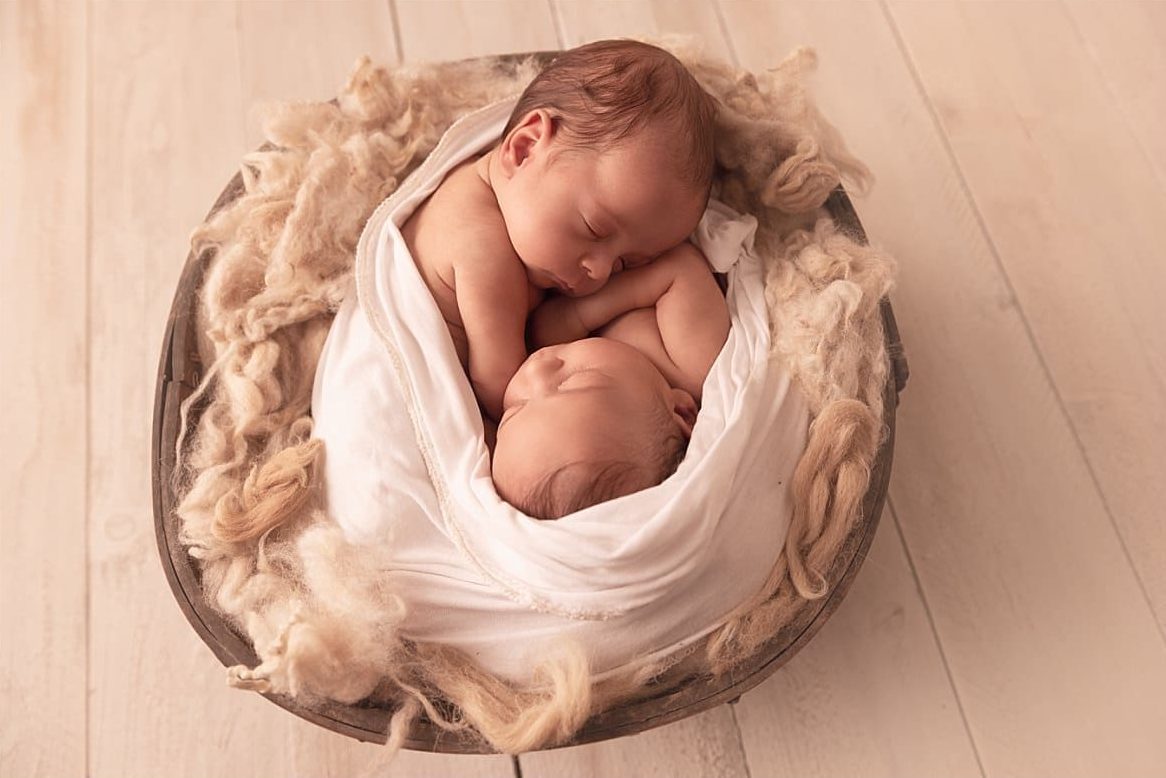 Deux nouveau-nés endormis dans un panier avec une couverture beige.